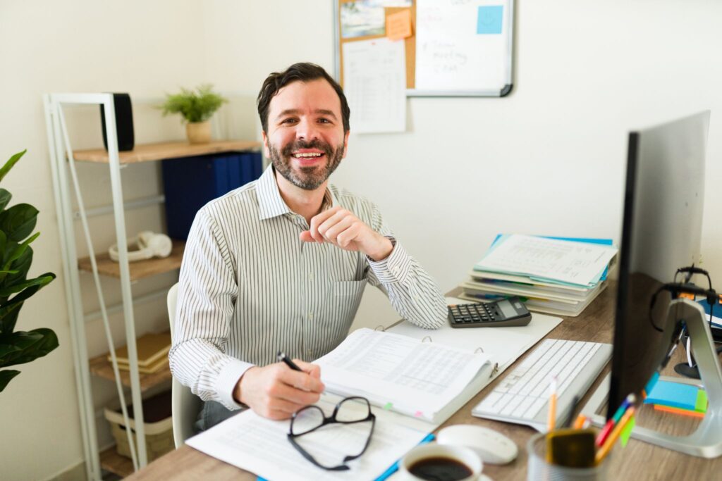 A smiling man sitting at his office desk working with documents.