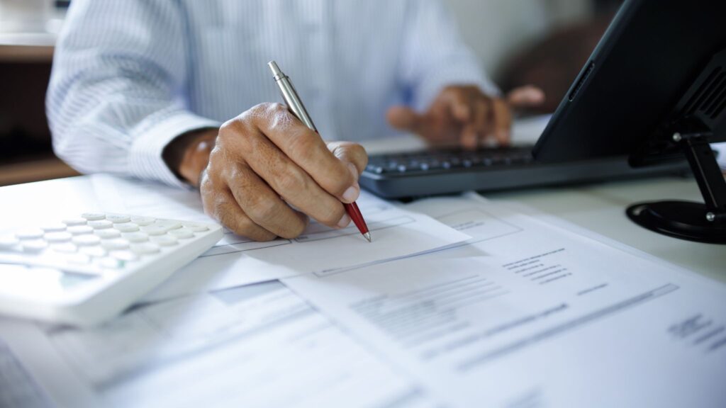 Close-up of a professional taking notes and filling out tax forms with a pen at a desk.