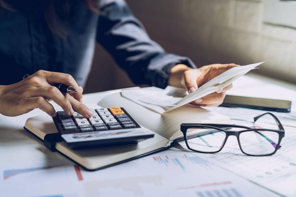 A focused businesswoman with glasses uses a calculator to assess financial figures amid paperwork