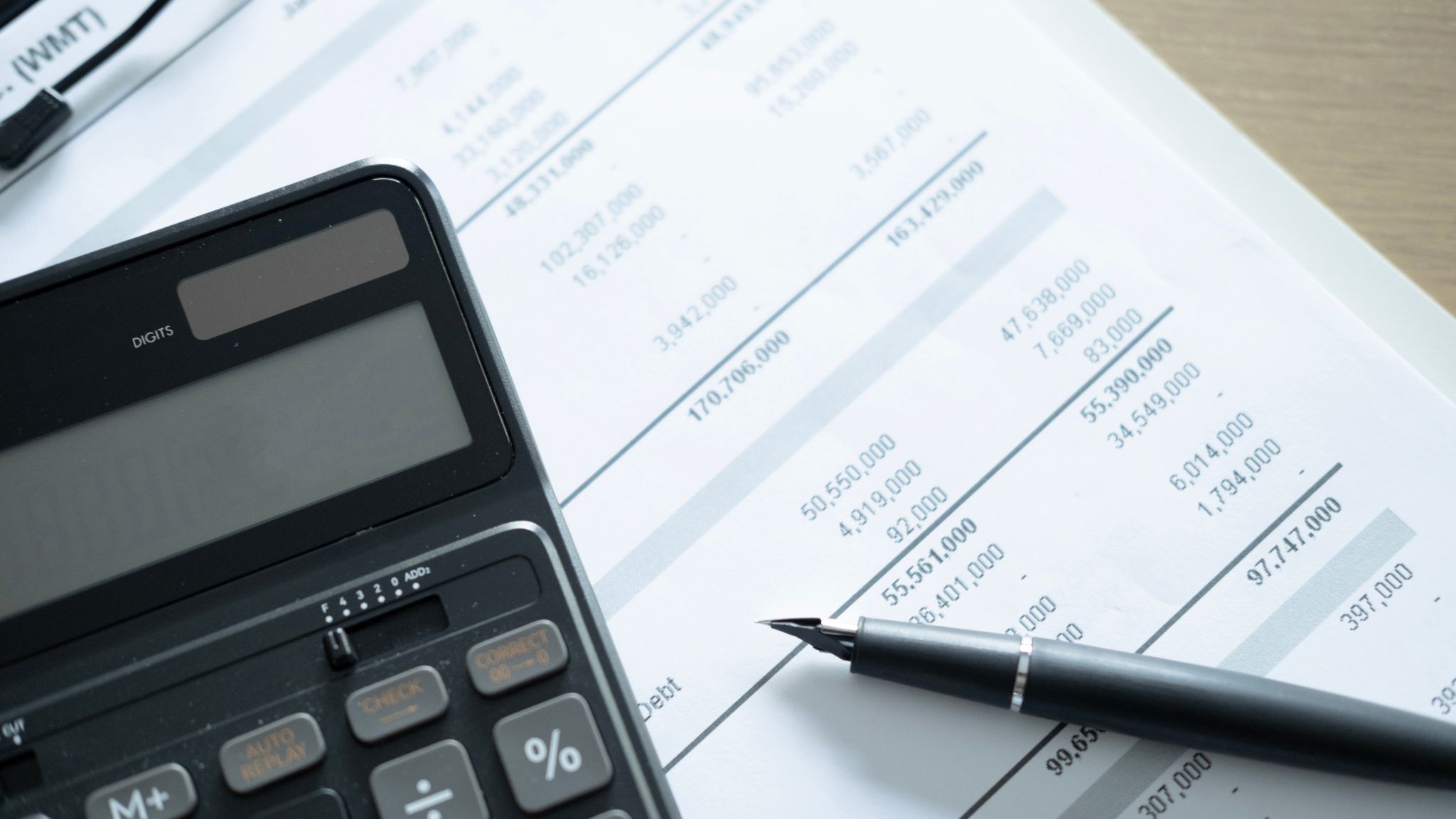 Black calculator and fountain pen resting on top of a financial document with rows of numbers.