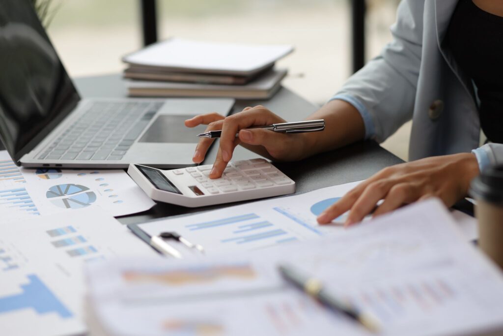 Accountant calculating financial data at a desk surrounded by laptop, reports, and charts.