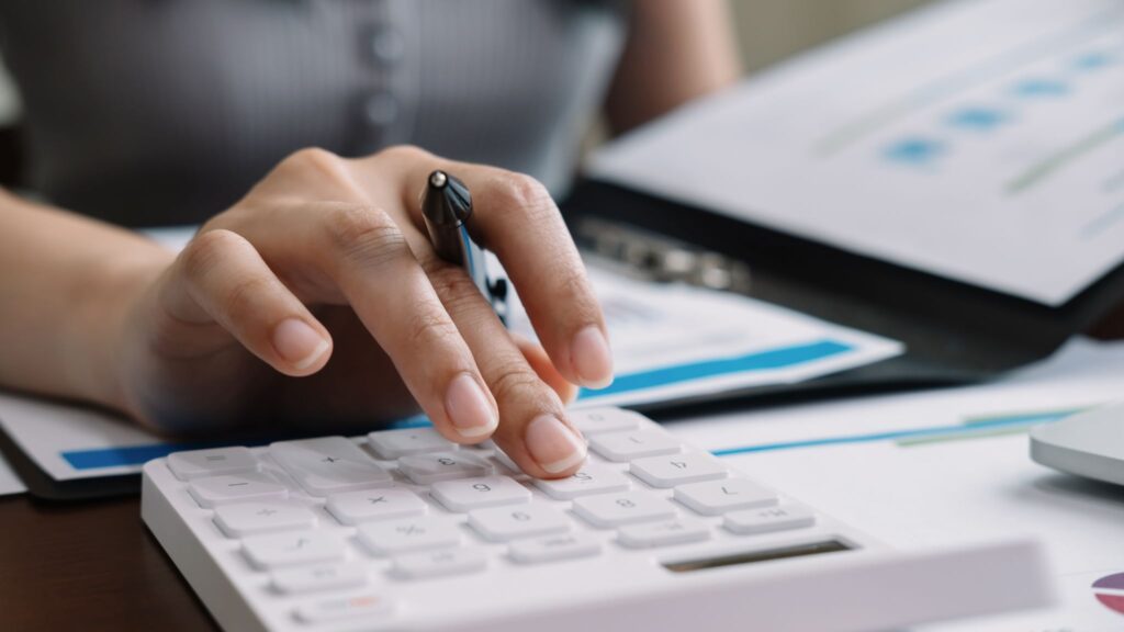 Close-up of a professional using a calculator with financial documents and charts on a desk.