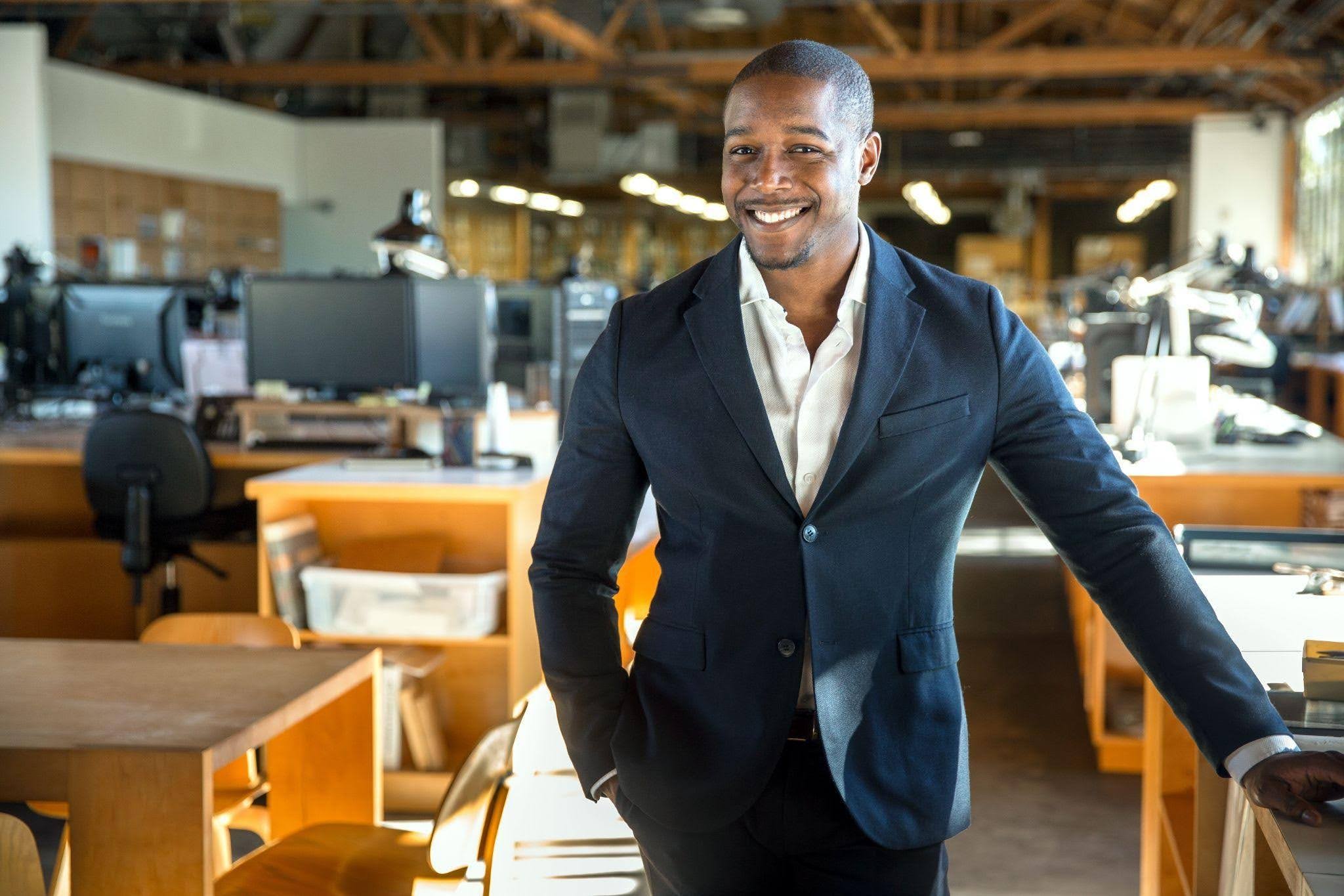 A professional man in a suit smiles while standing in a well lit office environment